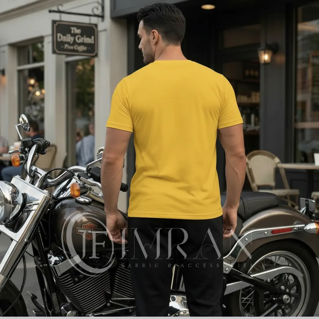 A male fashion model, for 'IF Imran Fabric ,' is shown posing on a vintage motorcycle parked on a city street outside a cafe with 'Daily Grind' signage. He is wearing the sun-kissed Gold t-shirt and black joggers set featuring the white crown and 'Live Like a King" text and Beard graphic.