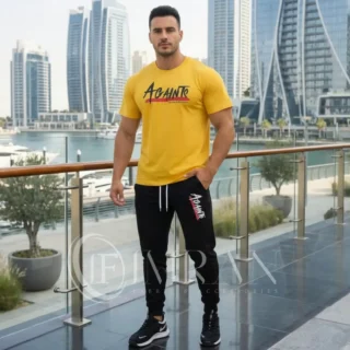 Model wearing Full 2-piece AGAINTS Urban Series Tracksuit fro men`s featuring a mustard yellow "AGAINTS" graphic t-shirt and onyx black joggers on th roof top of skyline buliding